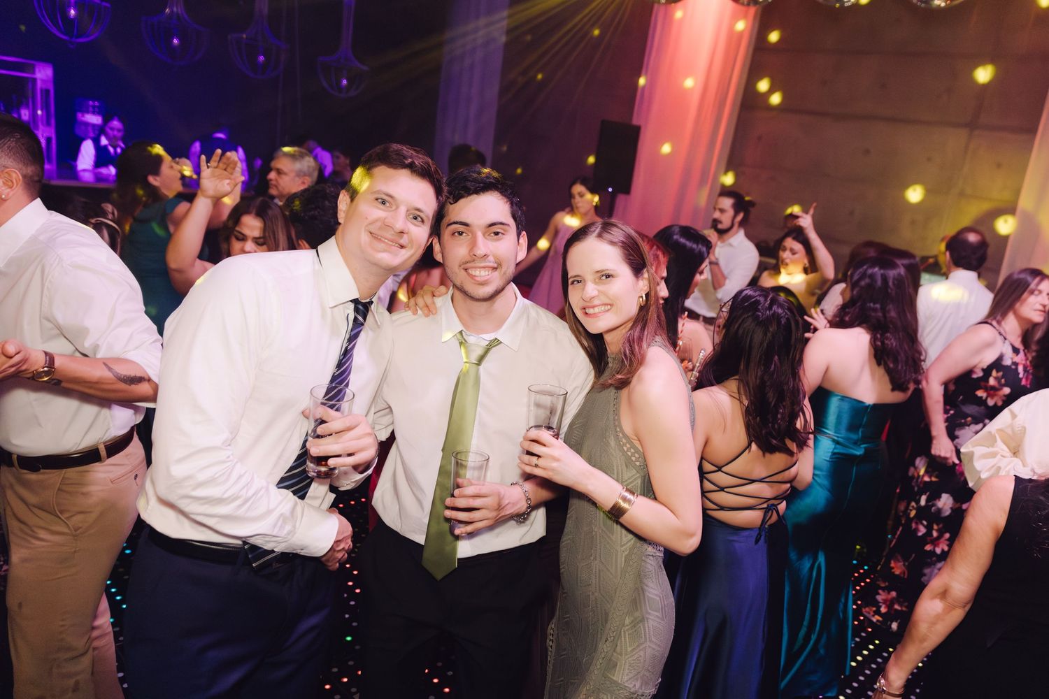 Three wedding guests smiling and posing together on dance floor at festive wedding reception.