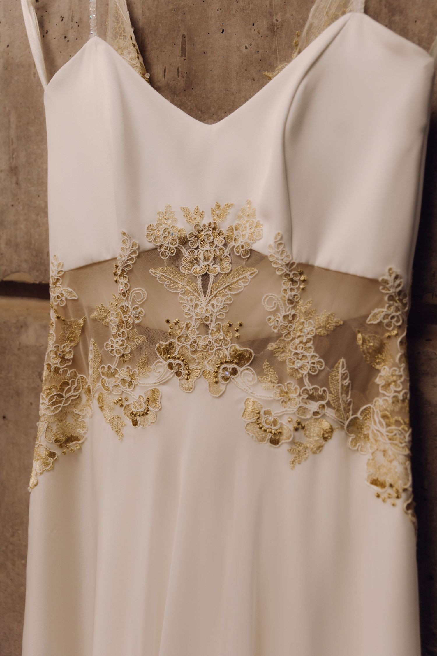 Close-up detail of white wedding dress featuring intricate gold lace embroidery at waist.