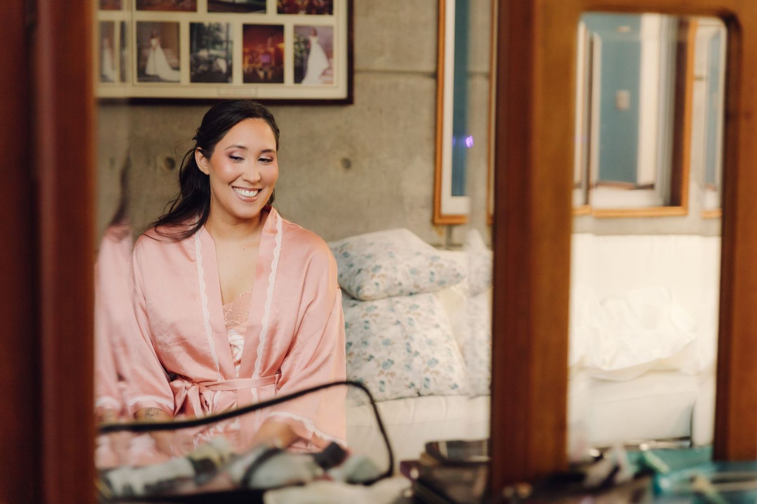 Bride in pink satin robe smiling while getting ready on her wedding day.