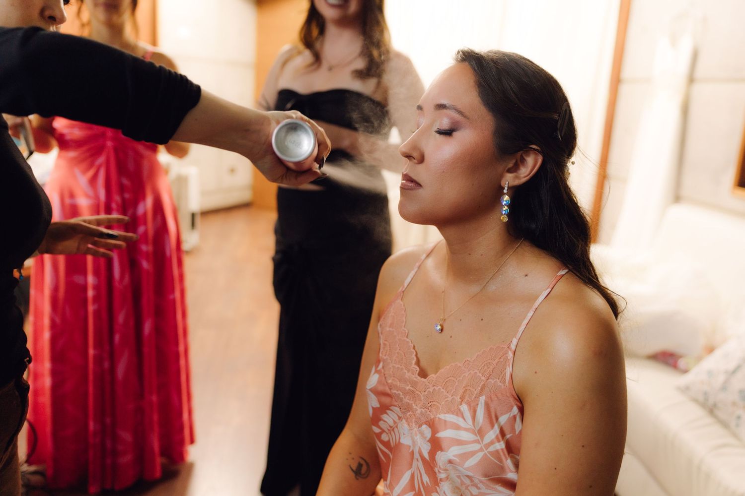 Makeup artist setting bridesmaid's makeup with spray while bridesmaids prepare for wedding ceremony.