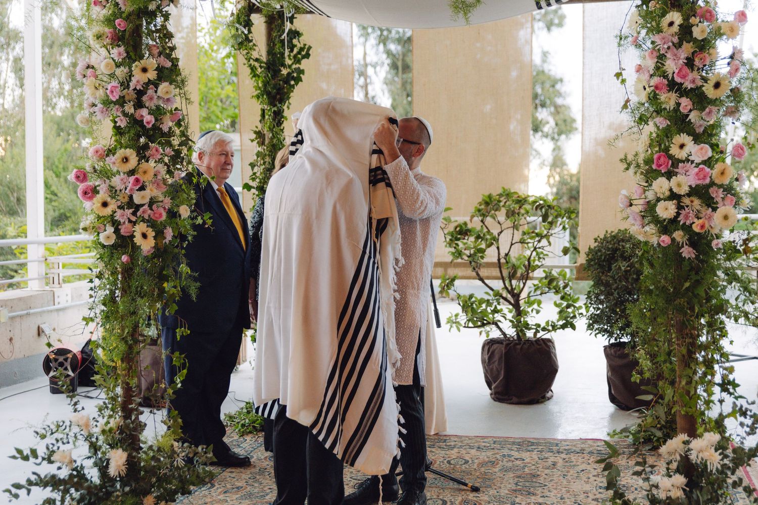 Couple shares intimate moment under tallit at decorated Jewish wedding chuppah.