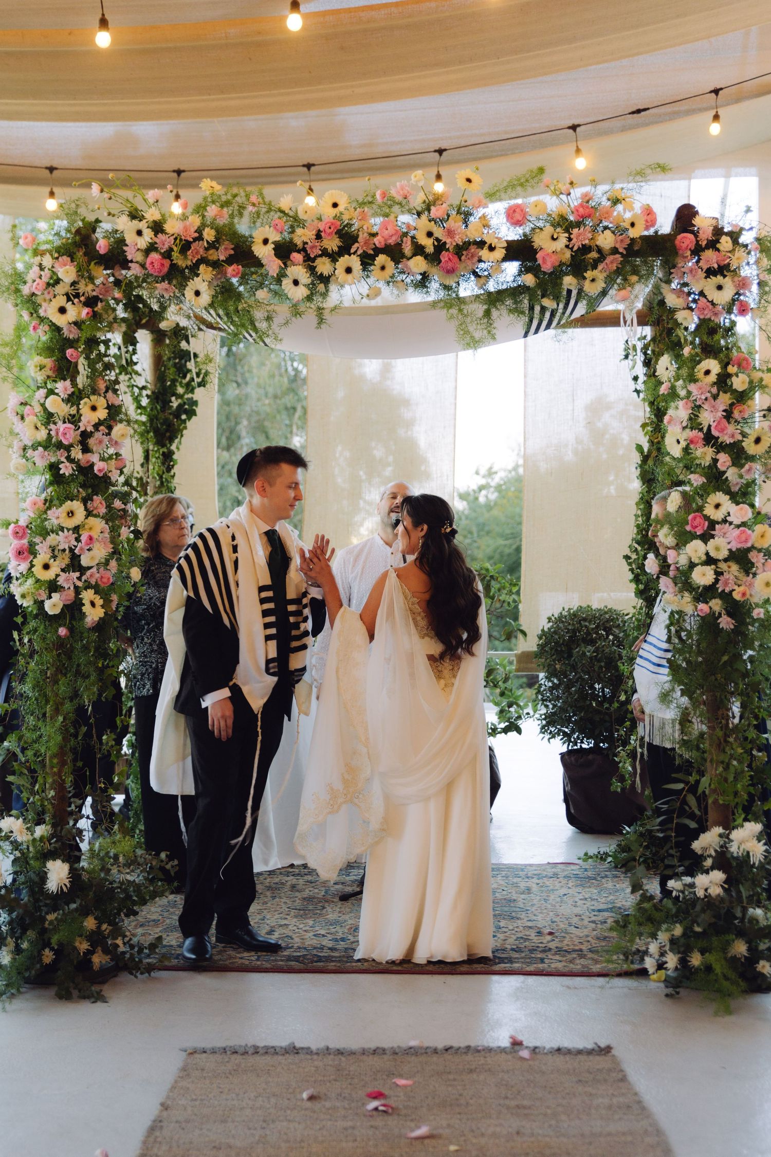 Bride and groom exchanging vows under flower-adorned chuppah at wedding.