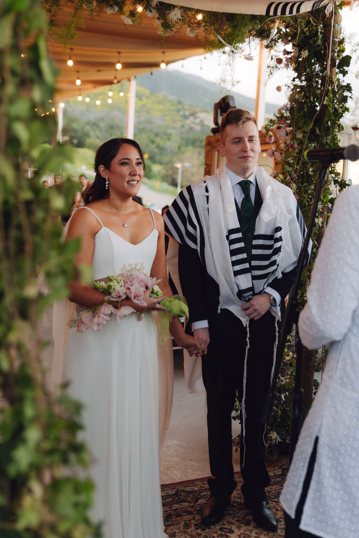 Smiling bride and groom standing together under chuppah at Jewish wedding.