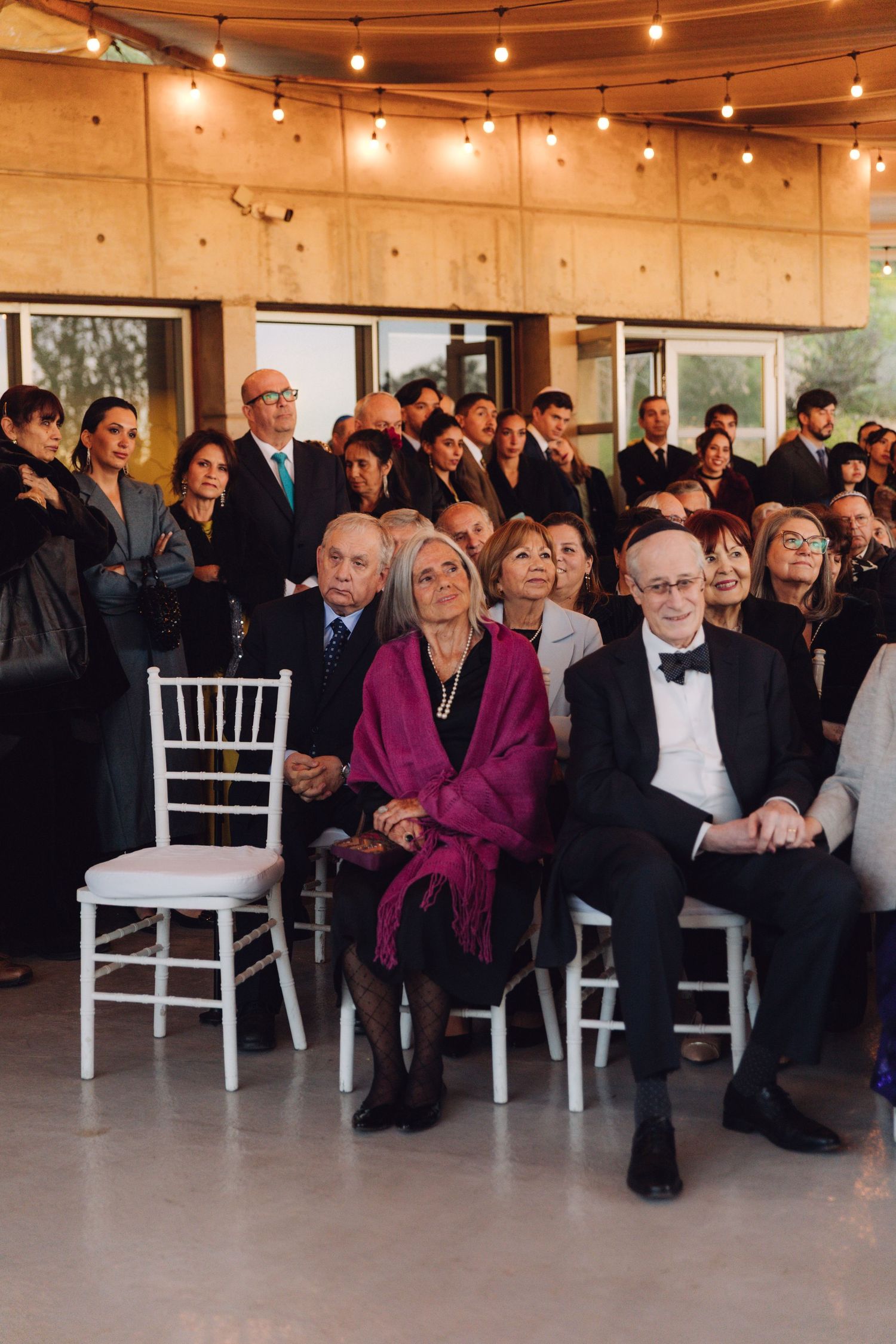 Guests seated and standing at an elegant Jewish wedding ceremony with string lights overhead.