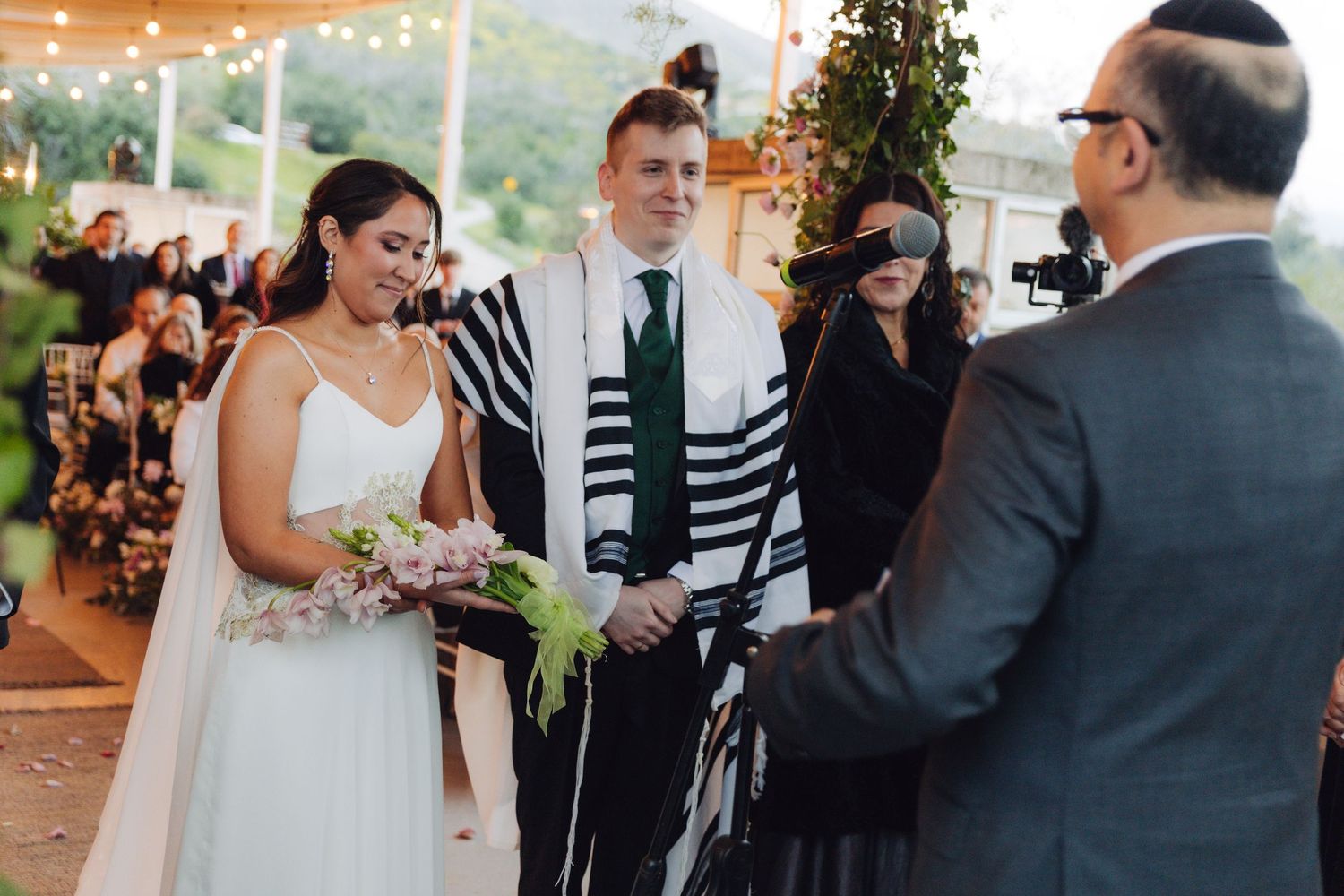 Bride and groom exchange vows under a chuppah at an outdoor Jewish wedding ceremony.