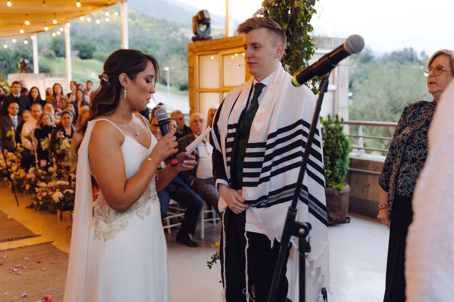 Bride reads her vows aloud to the groom during an outdoor Jewish wedding ceremony.