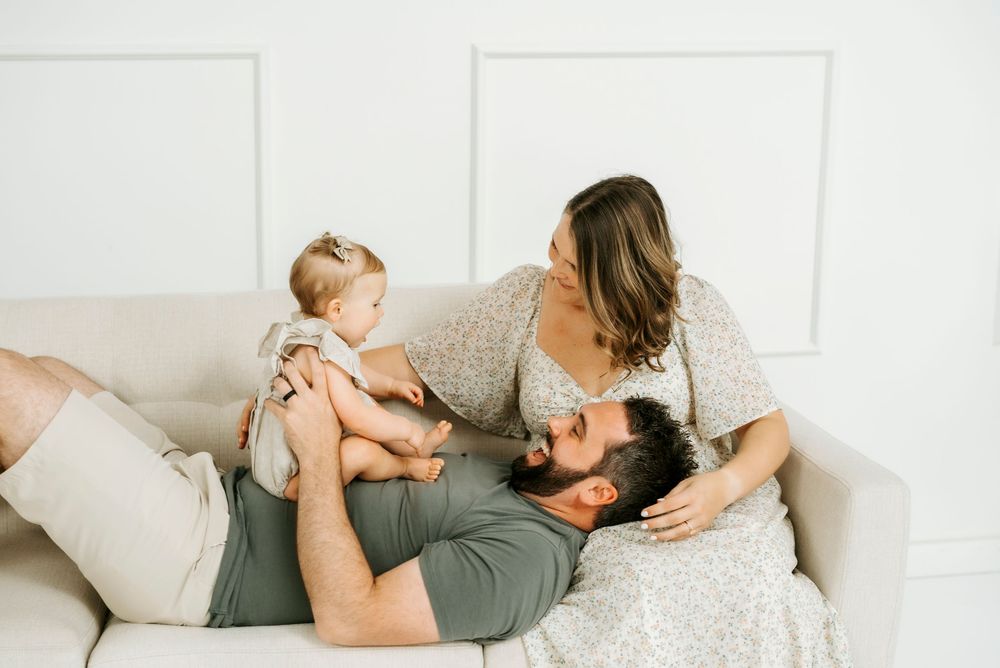 A young family with a baby relaxing on a white sofa in a bright, cozy living room setting.