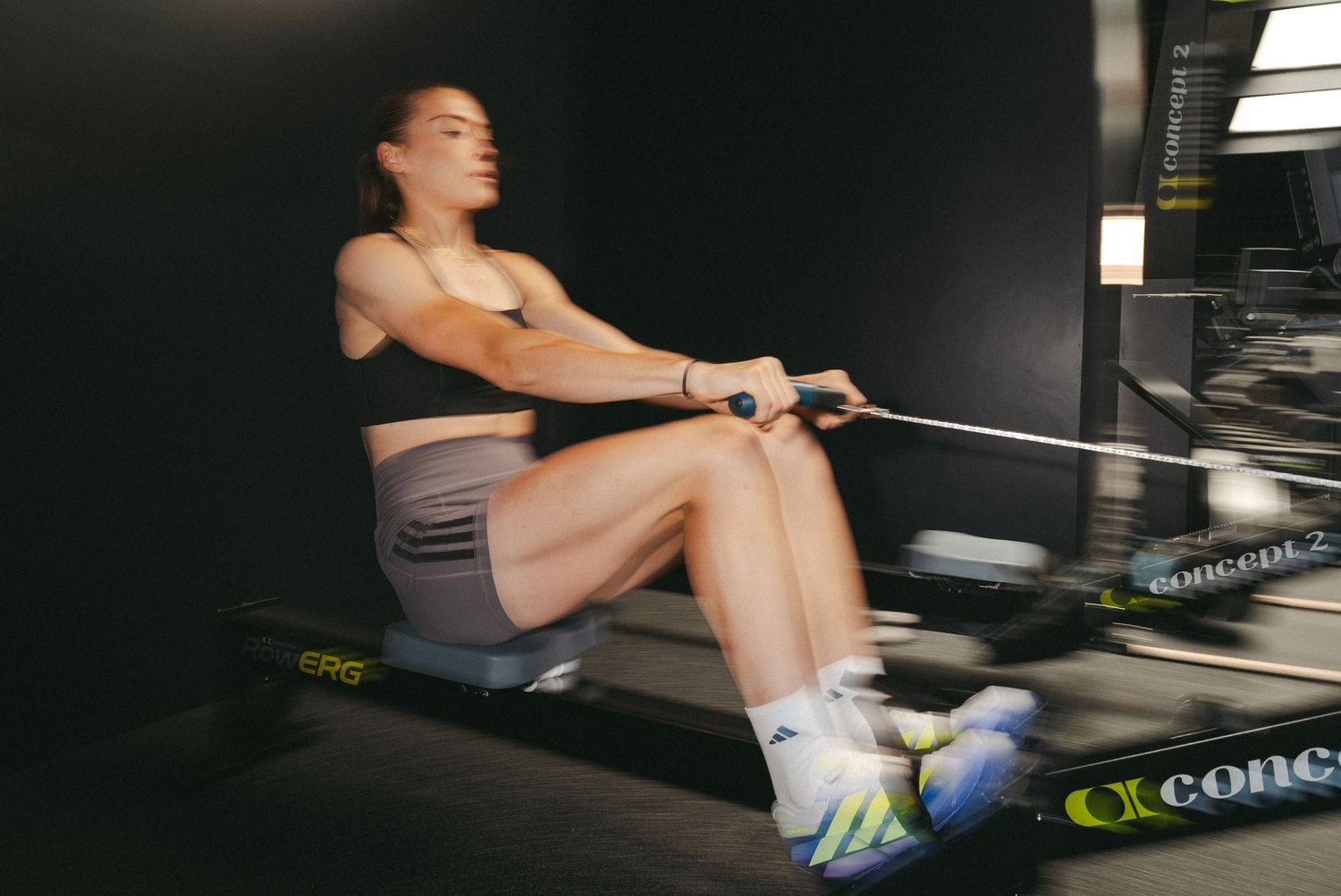 Woman intensely rowing on a Concept2 rowing machine during an indoor workout session.