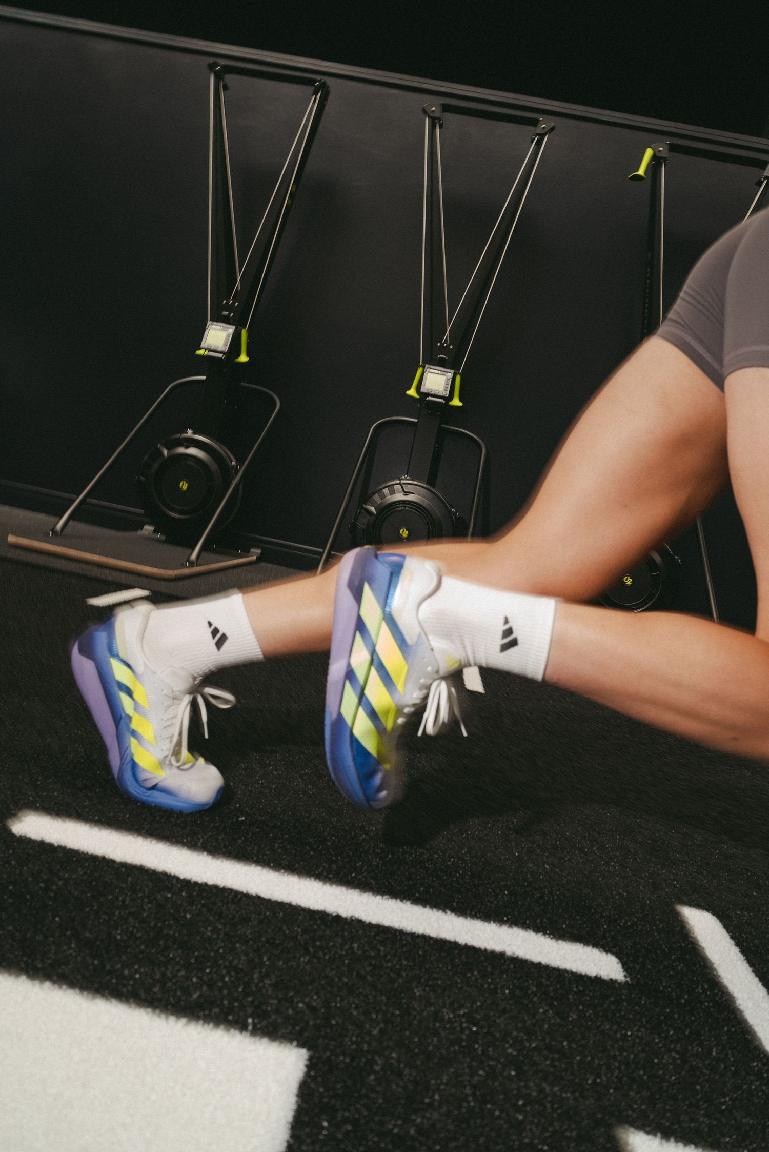 Person wearing colorful Adidas sneakers with yellow and blue accents on a gym floor near rowing machines.