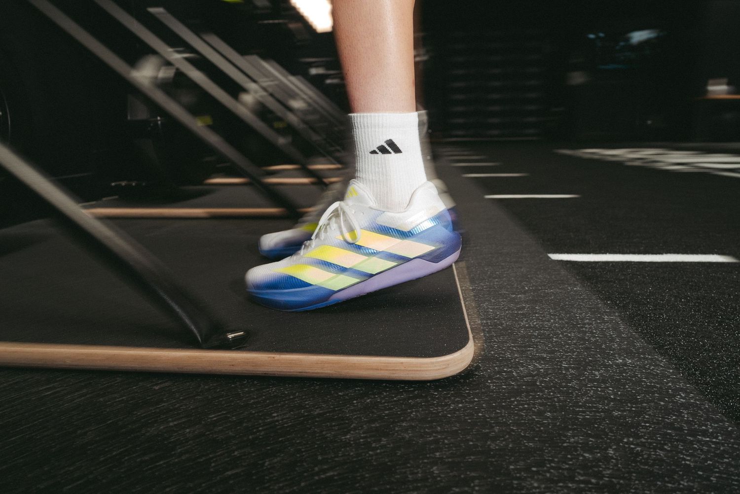 Close-up of a person wearing colorful Adidas sneakers with white socks on a treadmill in a gym.