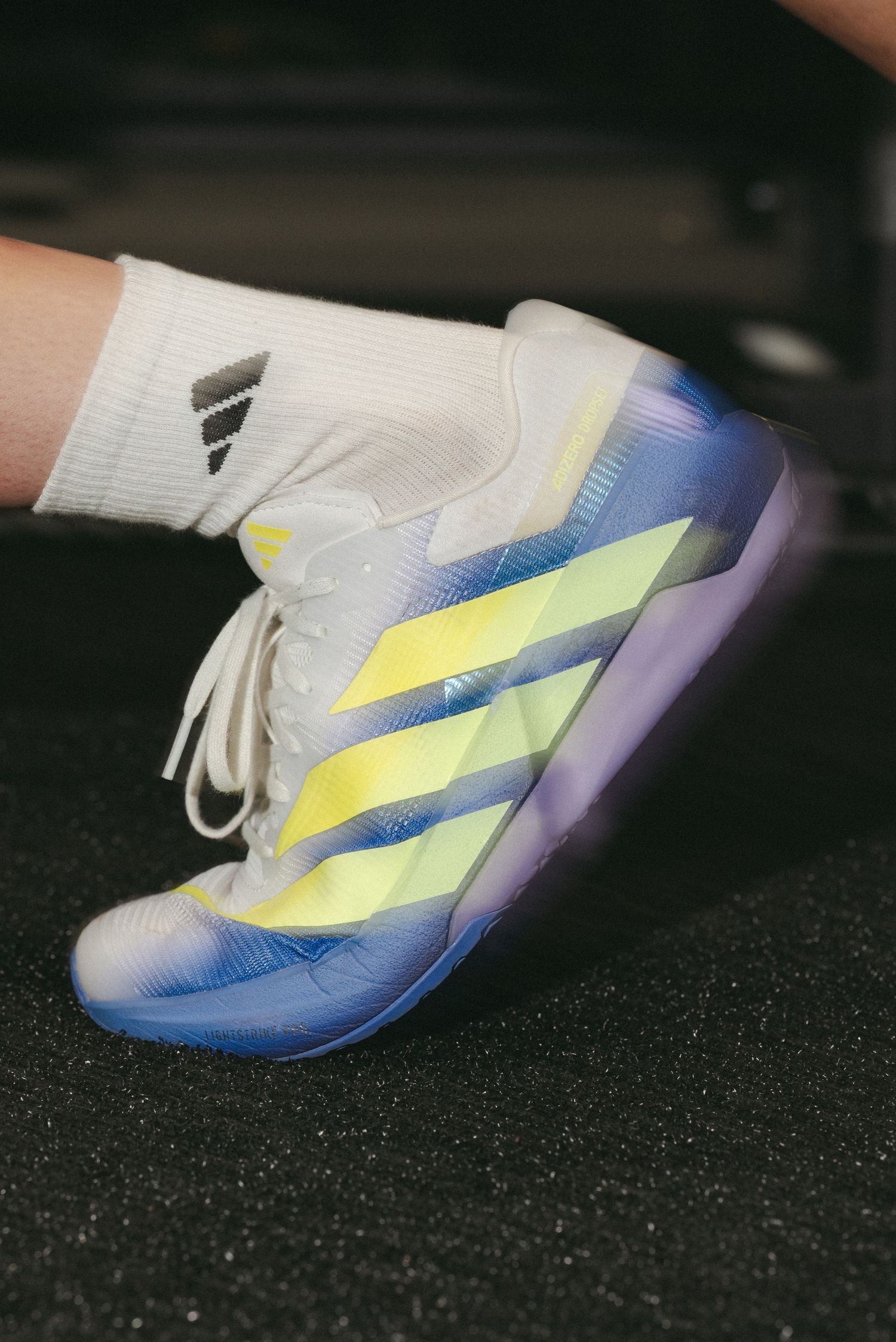 Close-up of Adidas HYROX athletic shoes featuring yellow stripes and purple sole on gym floor.