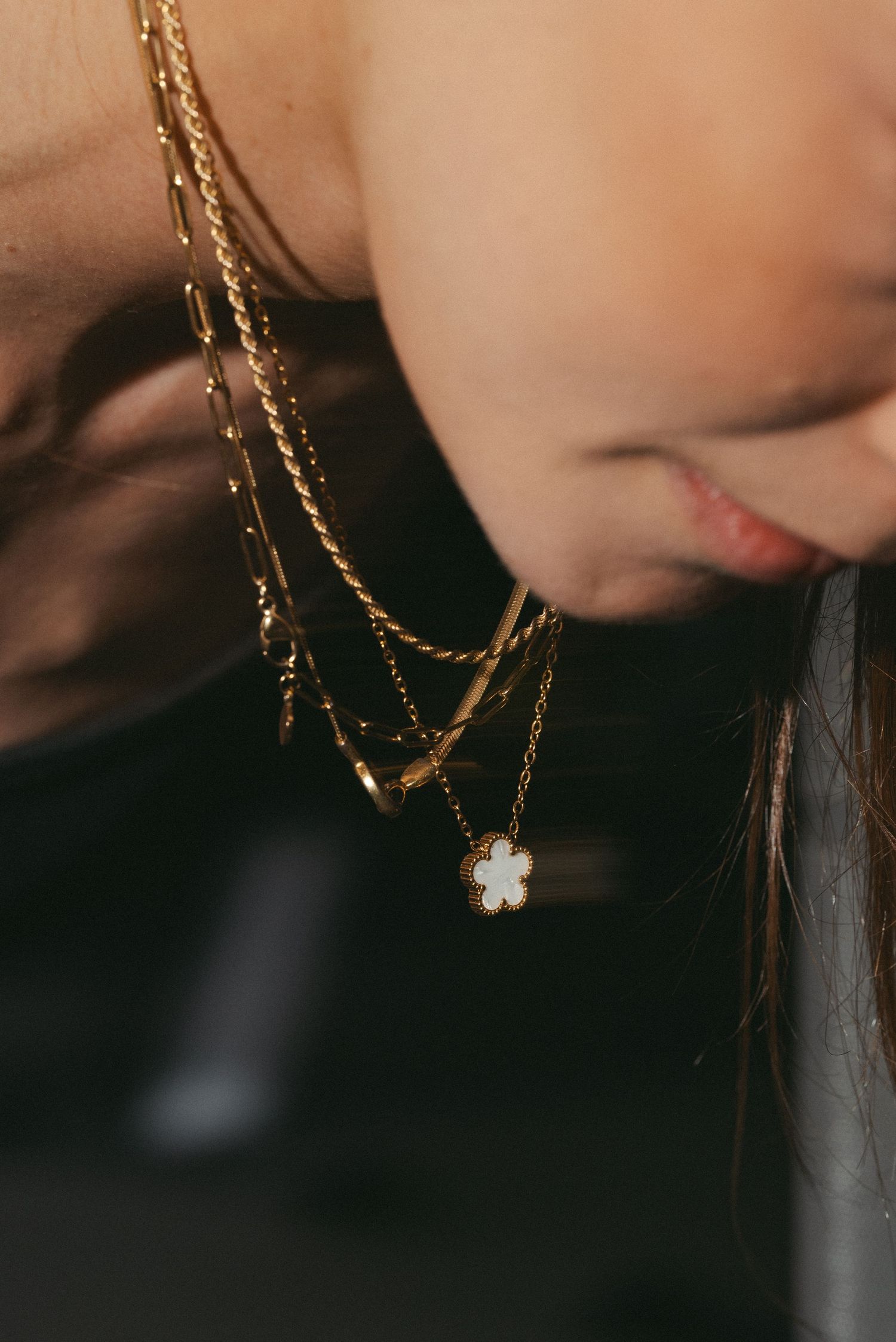Close-up of layered gold necklaces with a floral pendant on a woman.