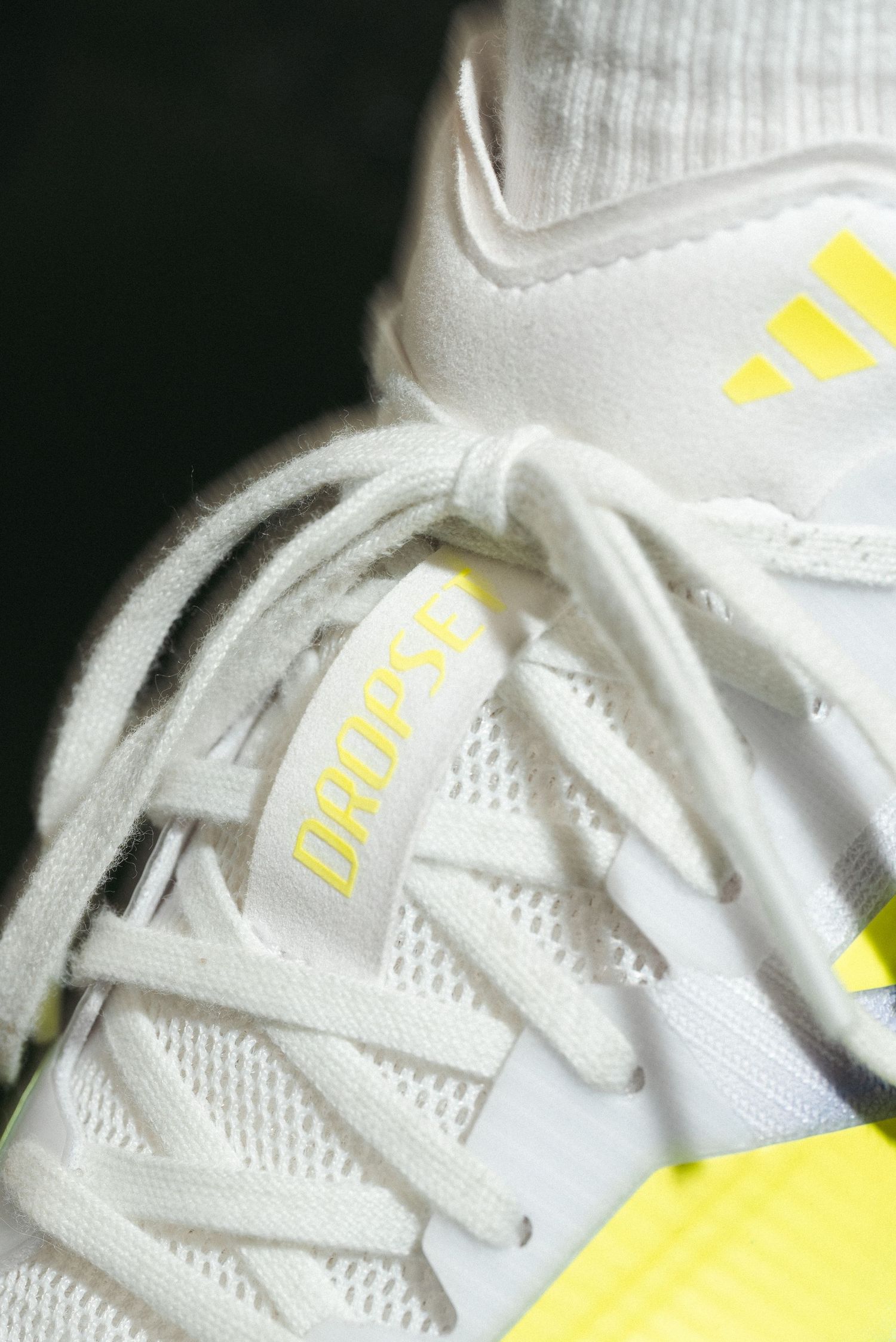 Close-up of white and yellow Adidas Dropset training shoes with bold yellow three-stripe logo detail.
