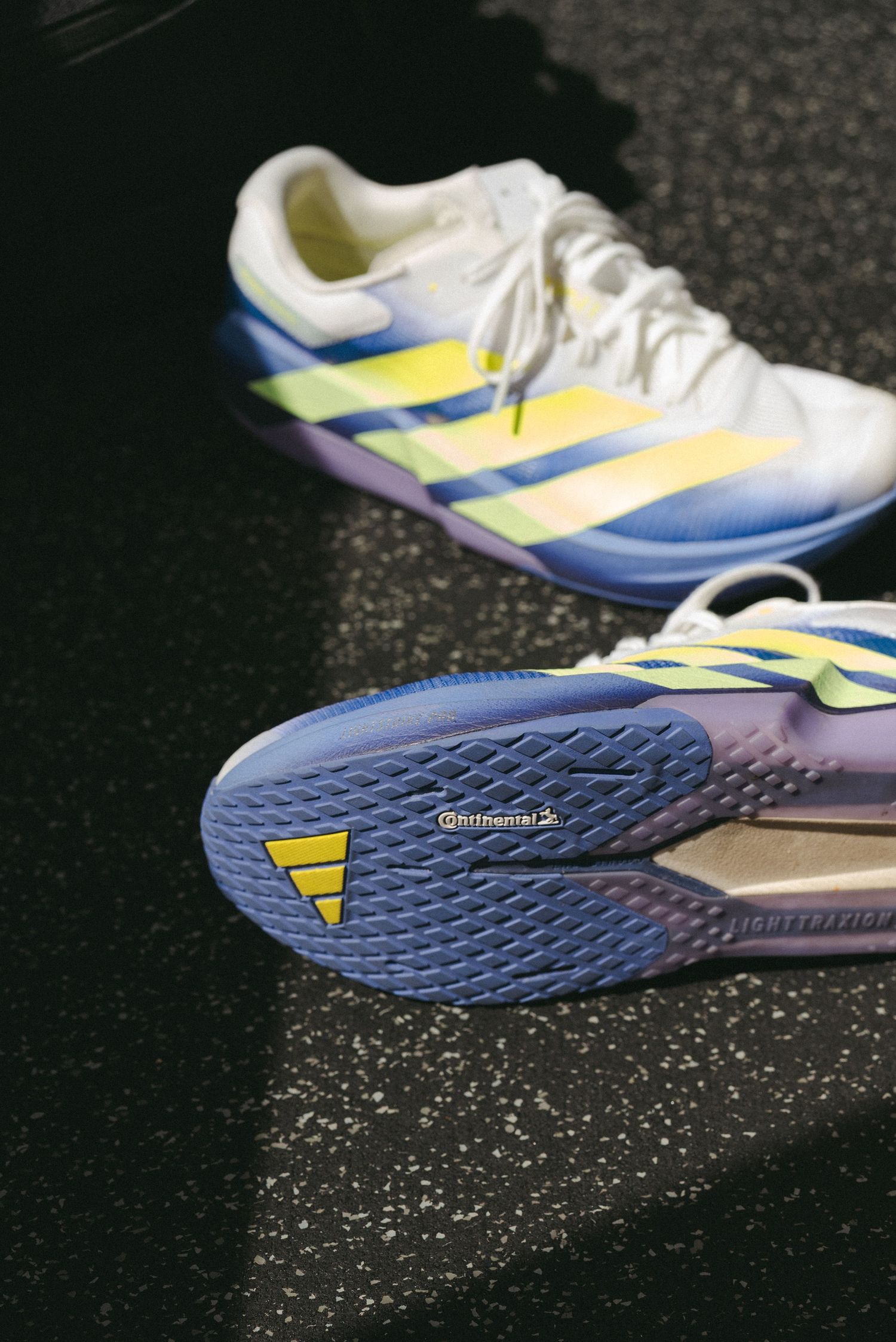 Adidas tennis shoes with yellow and blue stripes, featuring a purple Continental outsole on a dark surface.