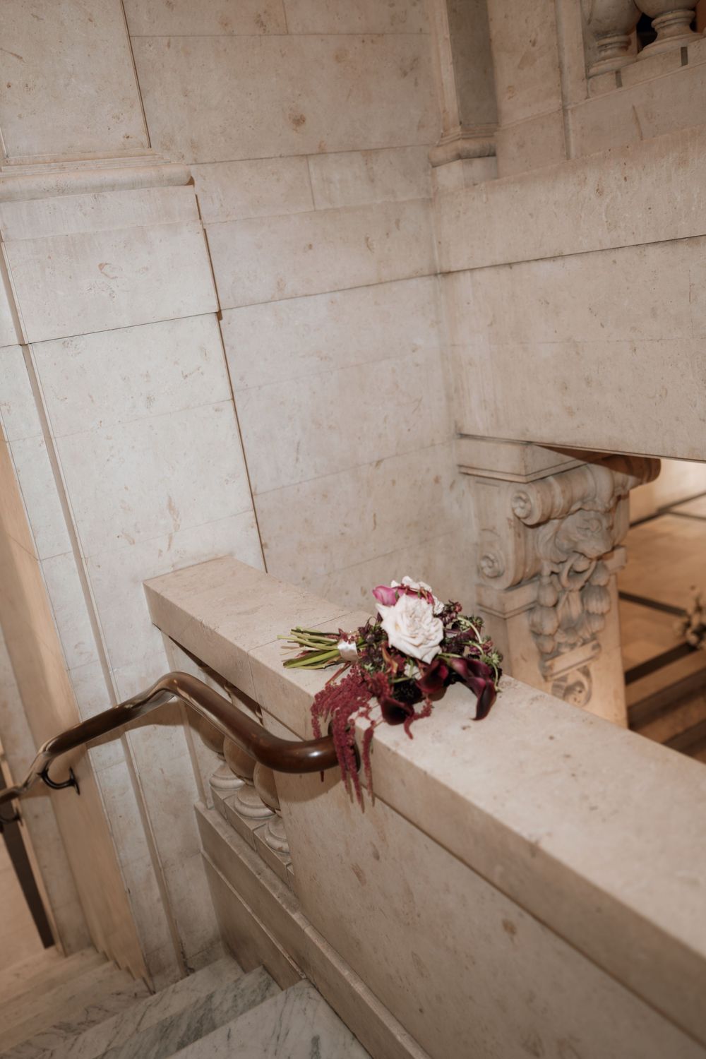 A bridal bouquet with white and burgundy flowers rests on marble staircase railing in an elegant venue.