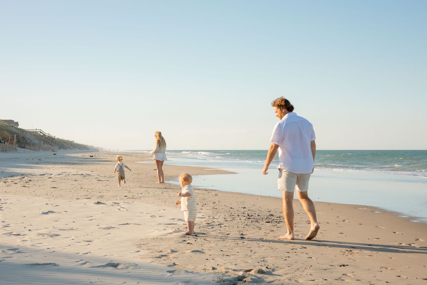 Black and white photo of a laughing couple holding hands and running barefoot on a beach, woman in white dress.