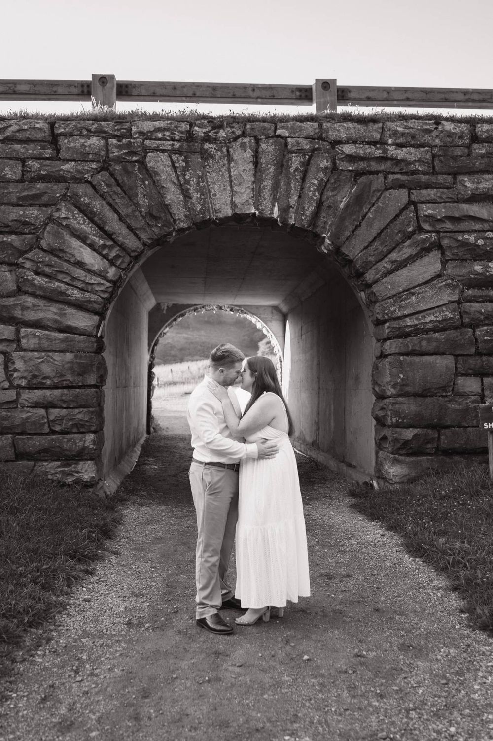 Black and white photo of couple sharing a kiss under a rustic stone arch tunnel outdoors, photographer Lexington NC
