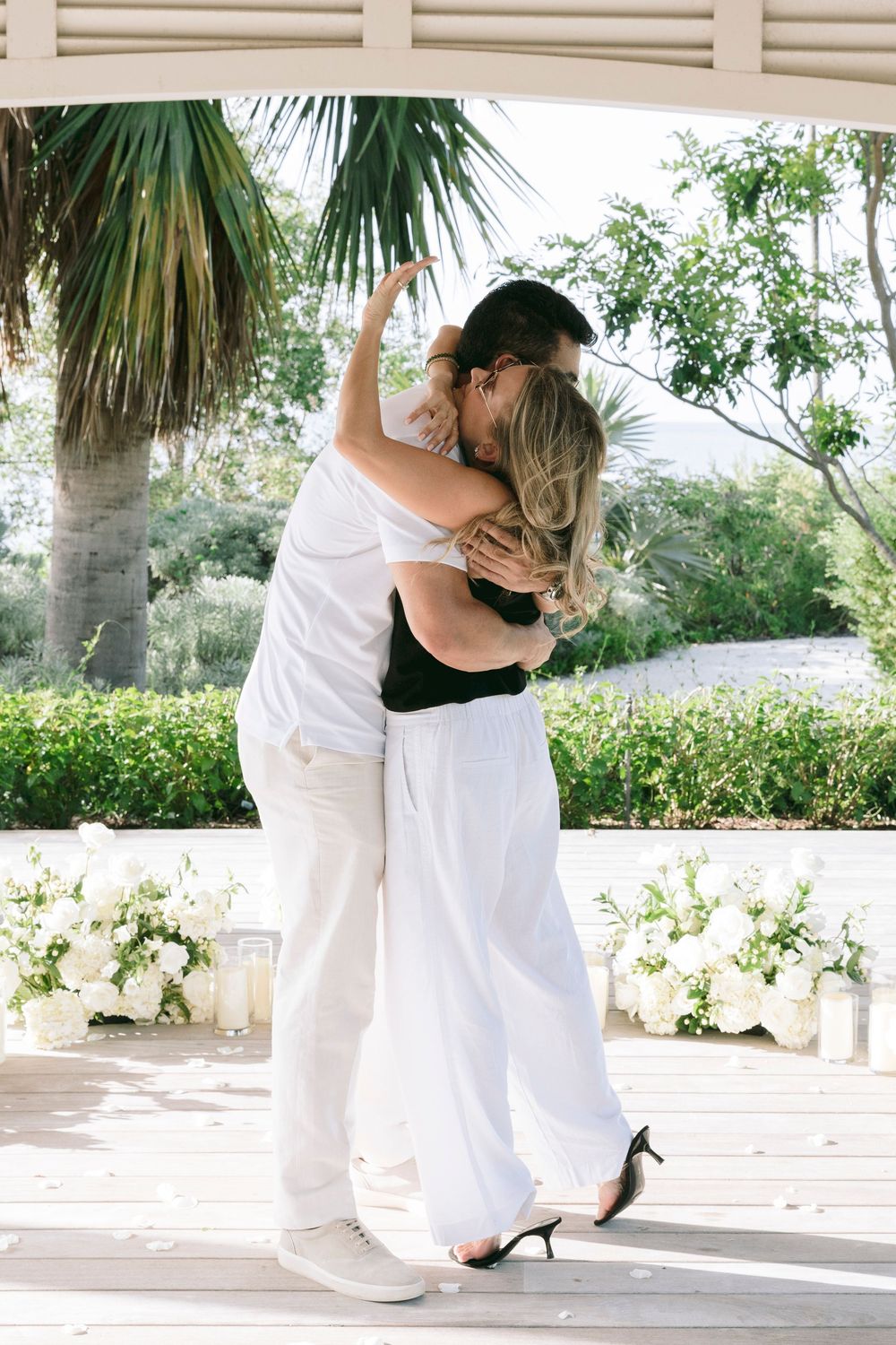 Couple sharing a romantic kiss under a pavilion surrounded by white floral arrangements at an outdoor wedding.