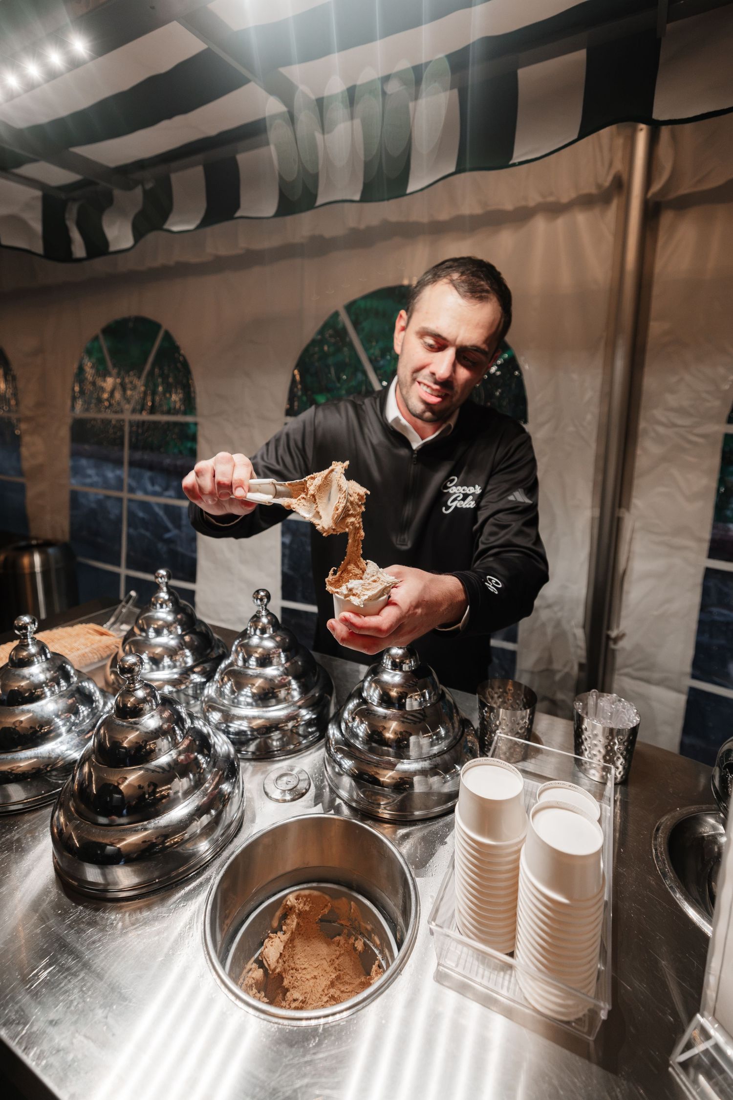 Smiling gelato vendor scooping ice cream into cups at an elegant outdoor wedding dessert station.