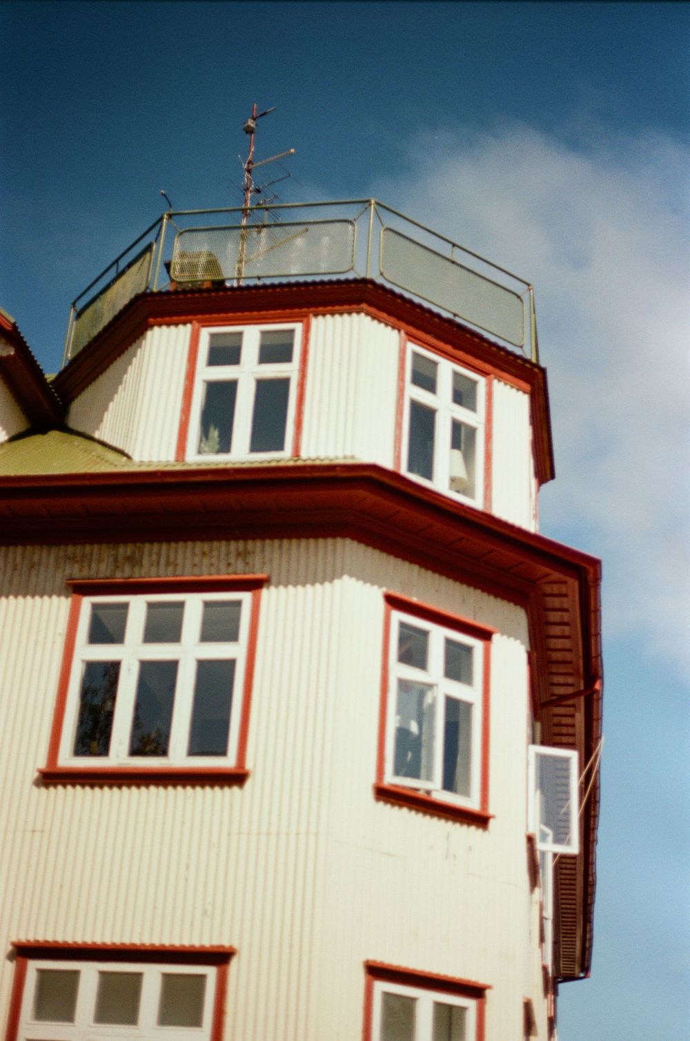 White and red trimmed building with observation deck and weather vane against a blue sky.