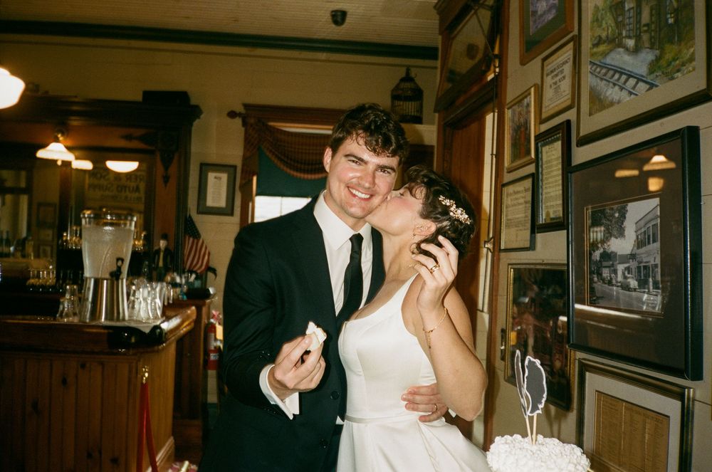 Happy newlywed couple sharing a kiss while cutting wedding cake in a cozy restaurant setting.