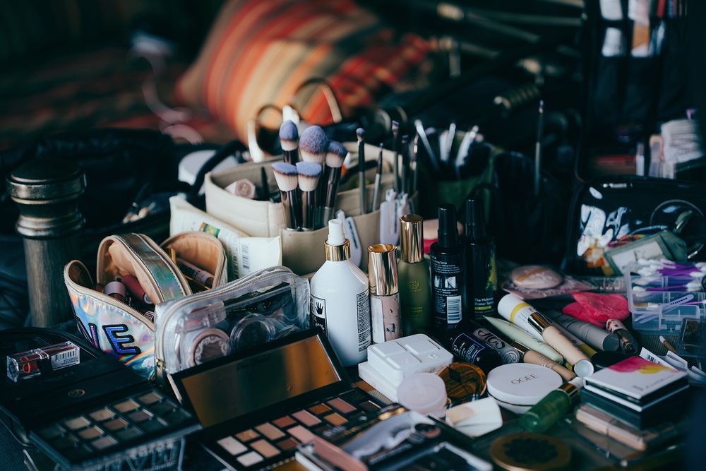 Cluttered makeup vanity with brushes, palettes, and beauty products organized in pouches and containers.