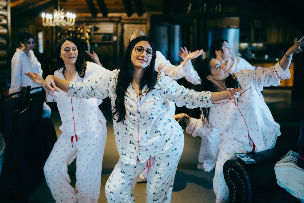 Group of women in matching white floral pajamas dancing and posing joyfully indoors at a festive gathering.