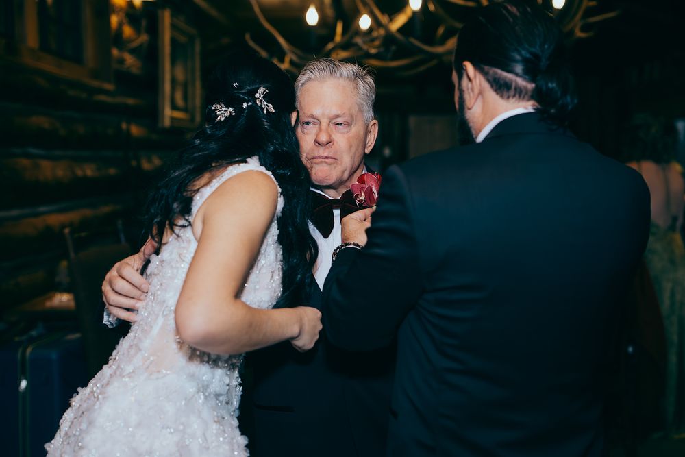Bride in white dress dancing with older man in tuxedo at elegant wedding reception.