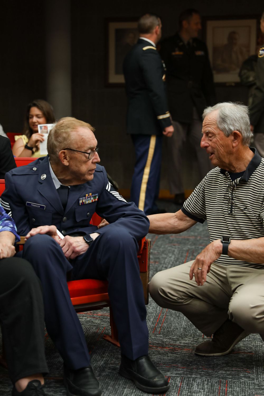 Two elderly veterans in military uniforms share a heartfelt conversation at a formal military ceremony event.