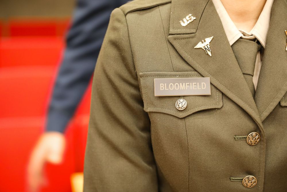 Close-up of military uniform with Bloomfield name tag, US Army insignia, and medical corps pin on olive green jacket.
