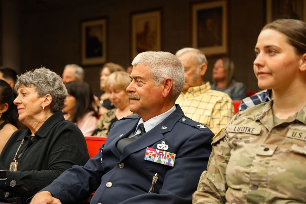 Military officers and civilians seated at a formal ceremony, featuring dress uniforms with medals and ribbons.