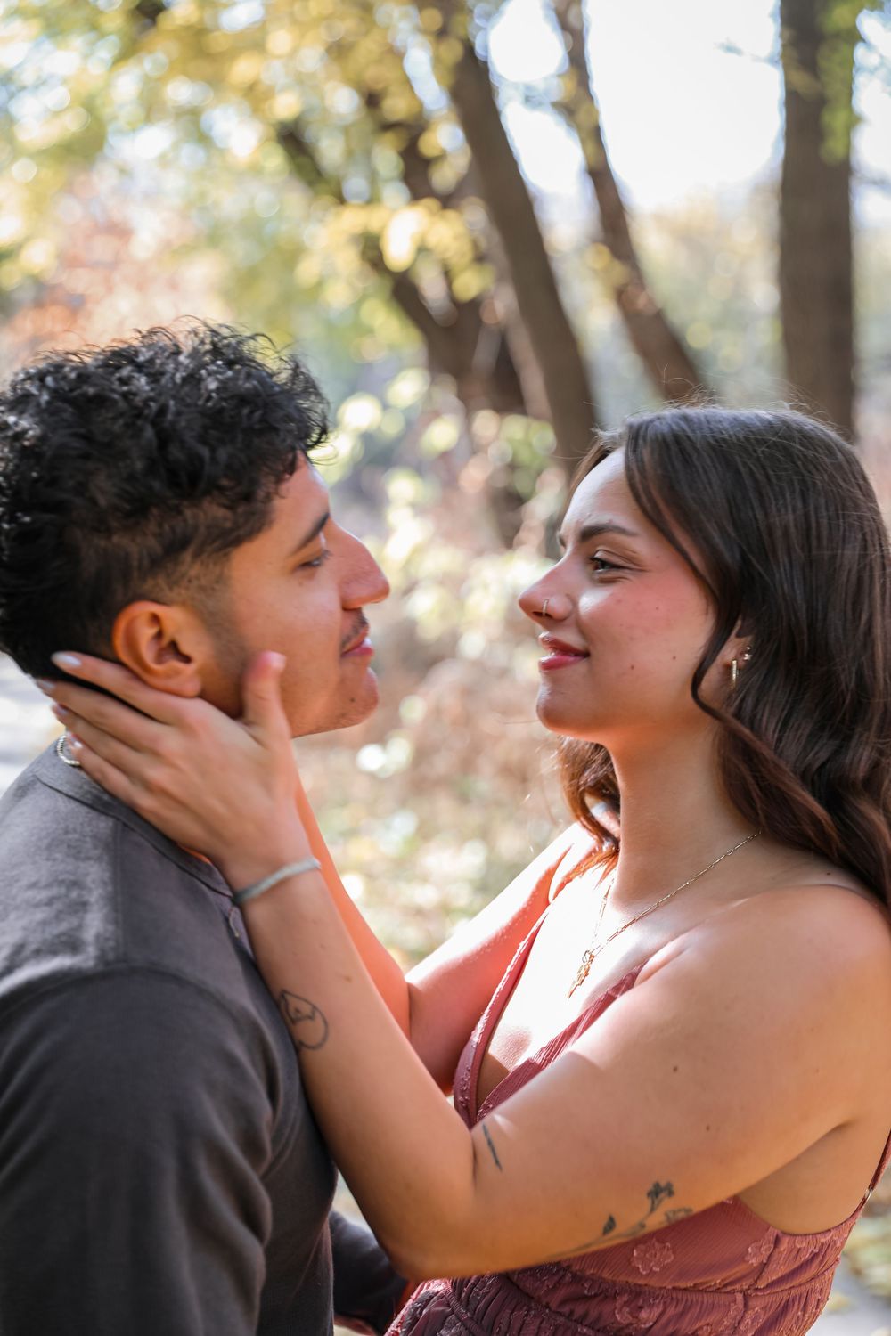 Young couple sharing a romantic moment outdoors, smiling at each other in a sunlit autumn park.