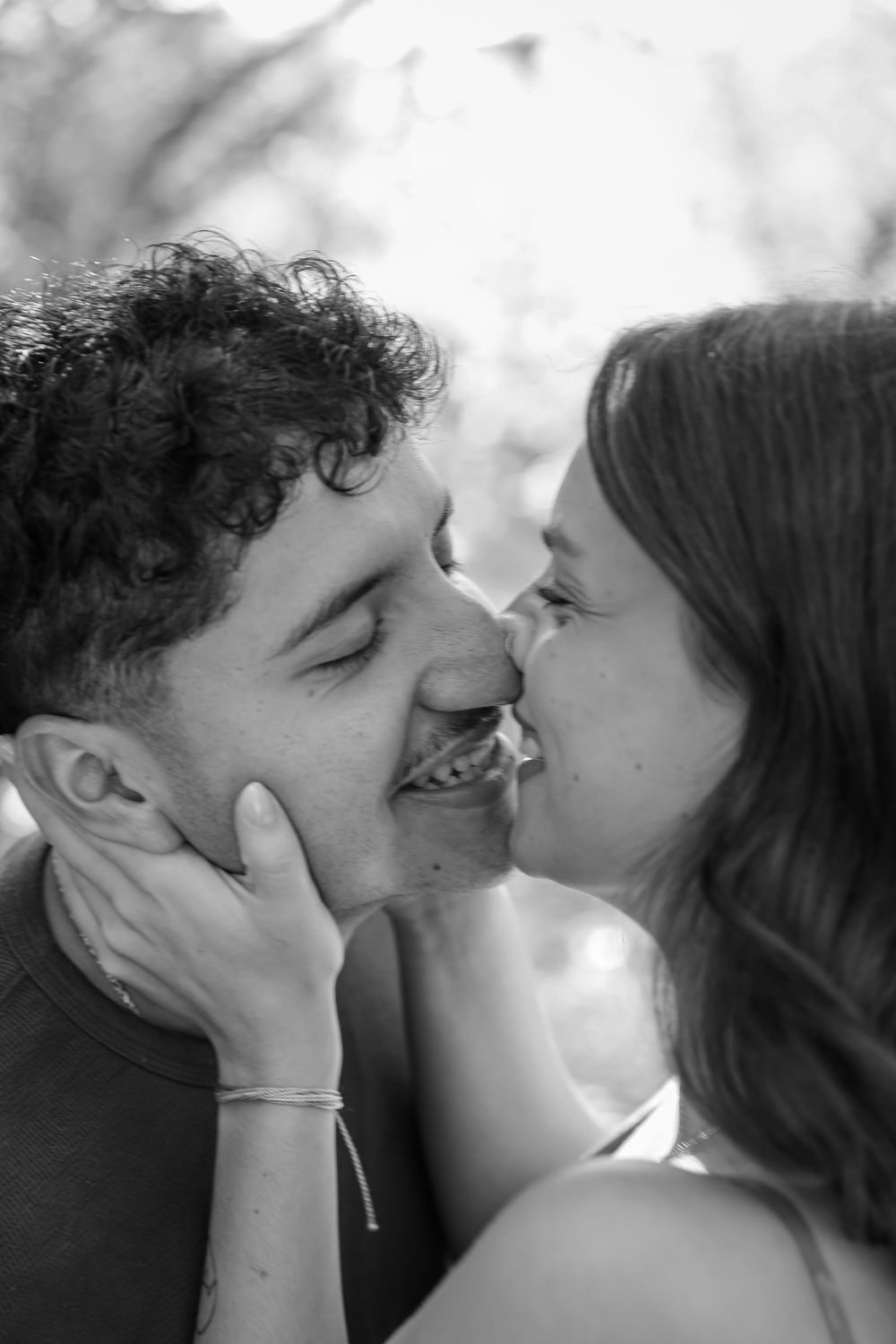 Black and white photo of a smiling couple sharing a tender kiss outdoors.