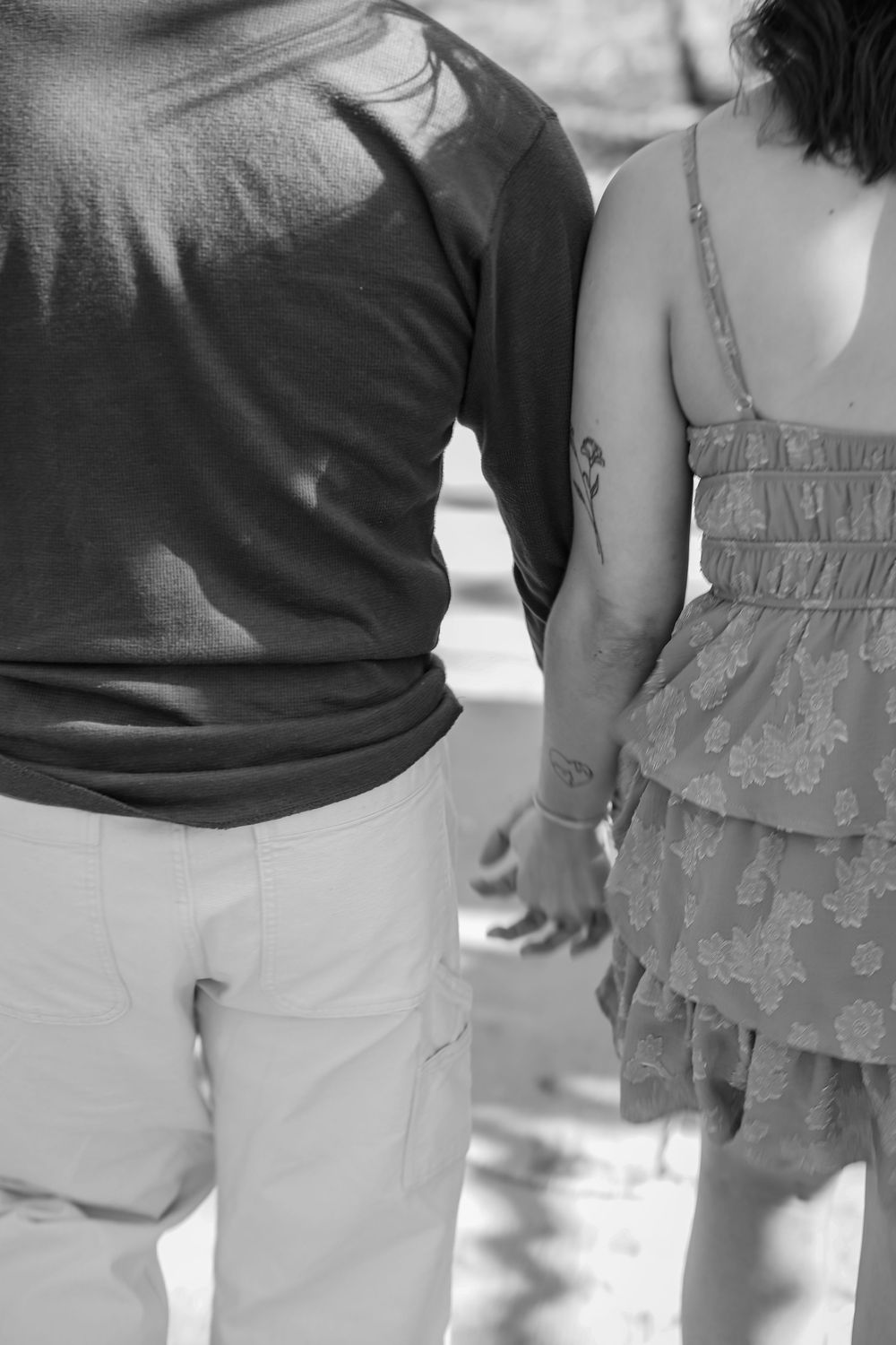 Black and white photo of a couple holding hands, viewed from behind, wearing casual summer clothing.