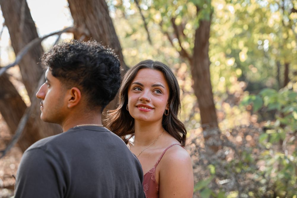 Young couple sharing a romantic moment outdoors in a sunlit forest, woman smiling warmly at her partner.