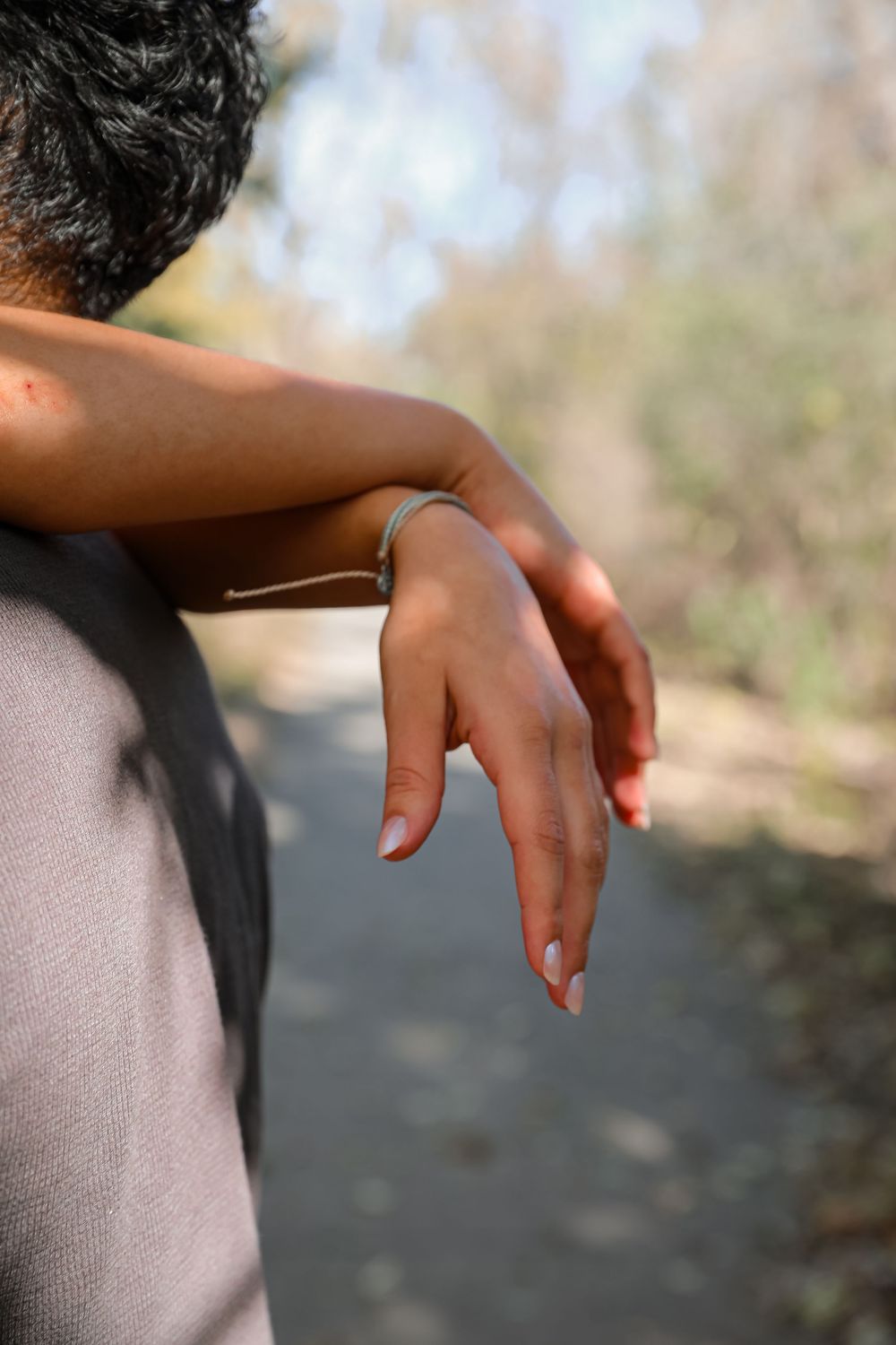 Close-up of a woman's hand with a delicate bracelet resting on a man's shoulder outdoors.