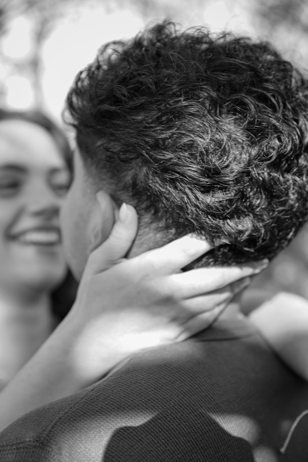 Black and white photo of a couple embracing, woman smiling with hand on mans curly hair.