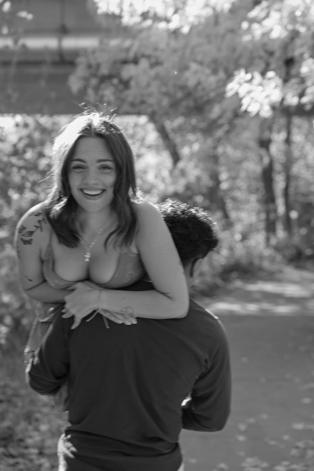 Black and white photo of a smiling woman getting a piggyback ride outdoors among trees.