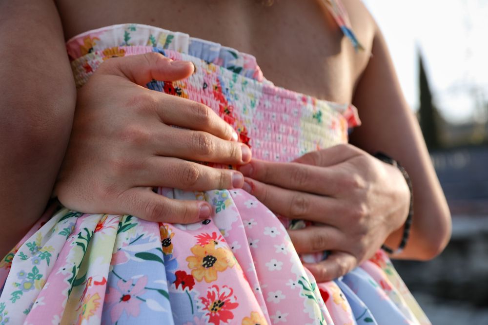 Close-up of hands adjusting a colorful floral smocked dress with pink, yellow, and blue flowers.