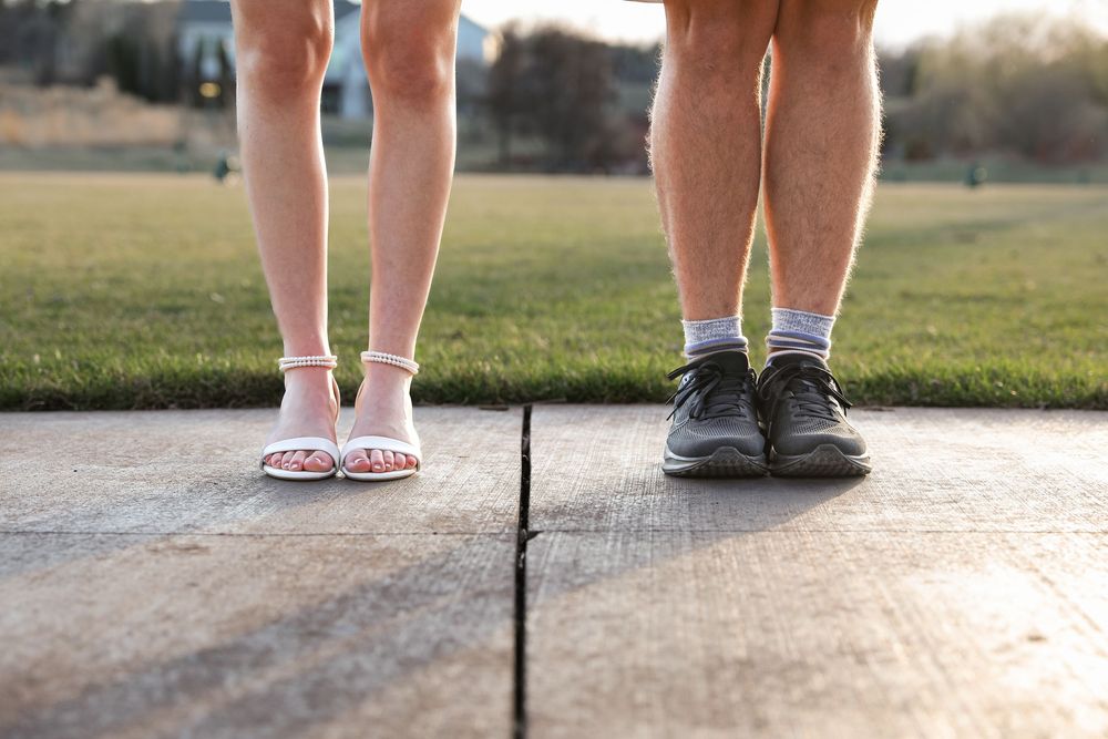 Close-up of two people standing on a wooden deck, one wearing sandals and one wearing sneakers with socks.
