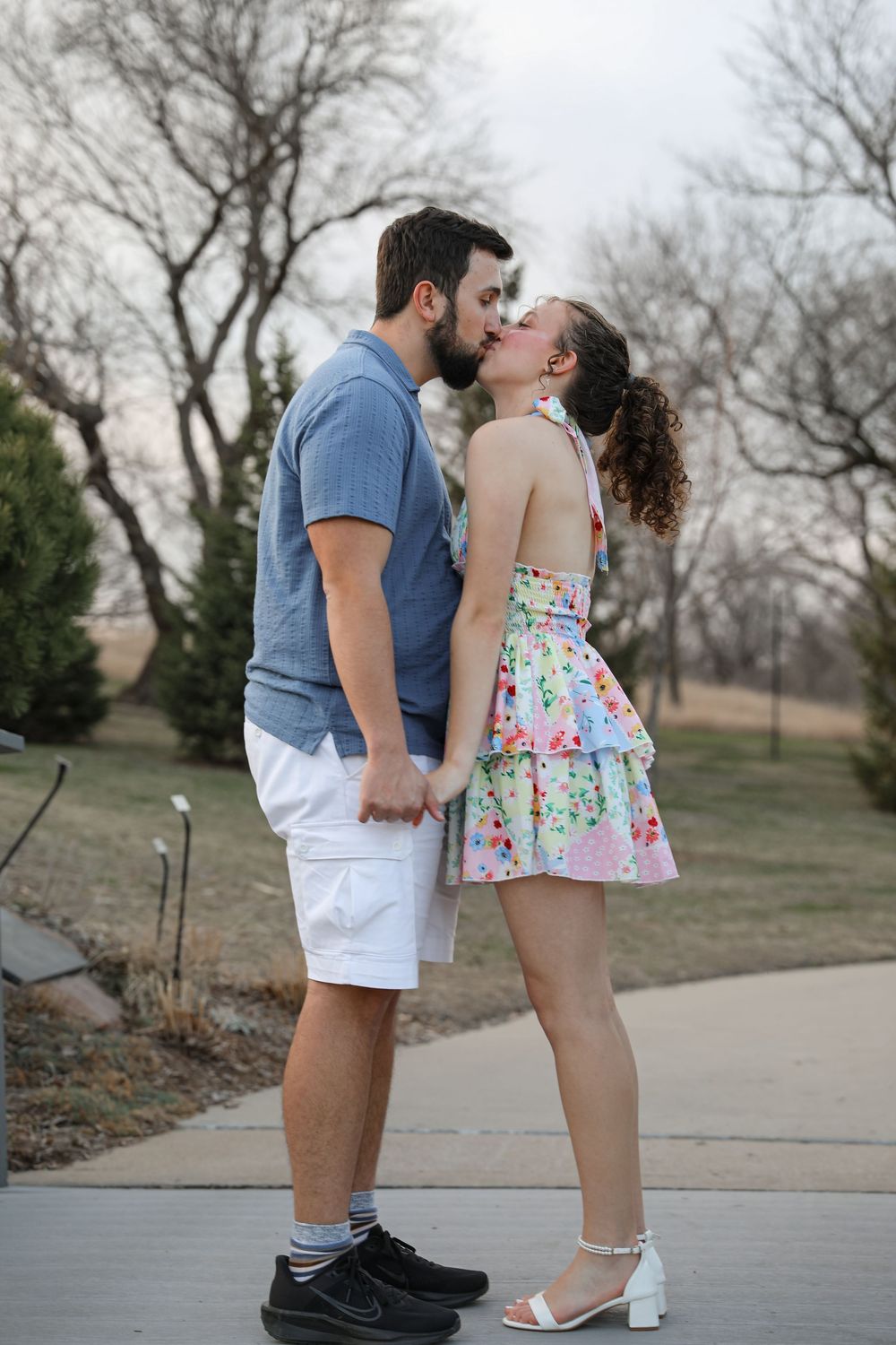A romantic couple shares a kiss while holding hands on an outdoor pathway.