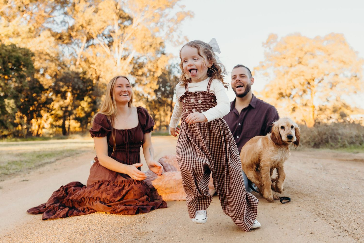 Happy young family with a toddler and golden retriever dog enjoying a sunny outdoor session on a dirt path.