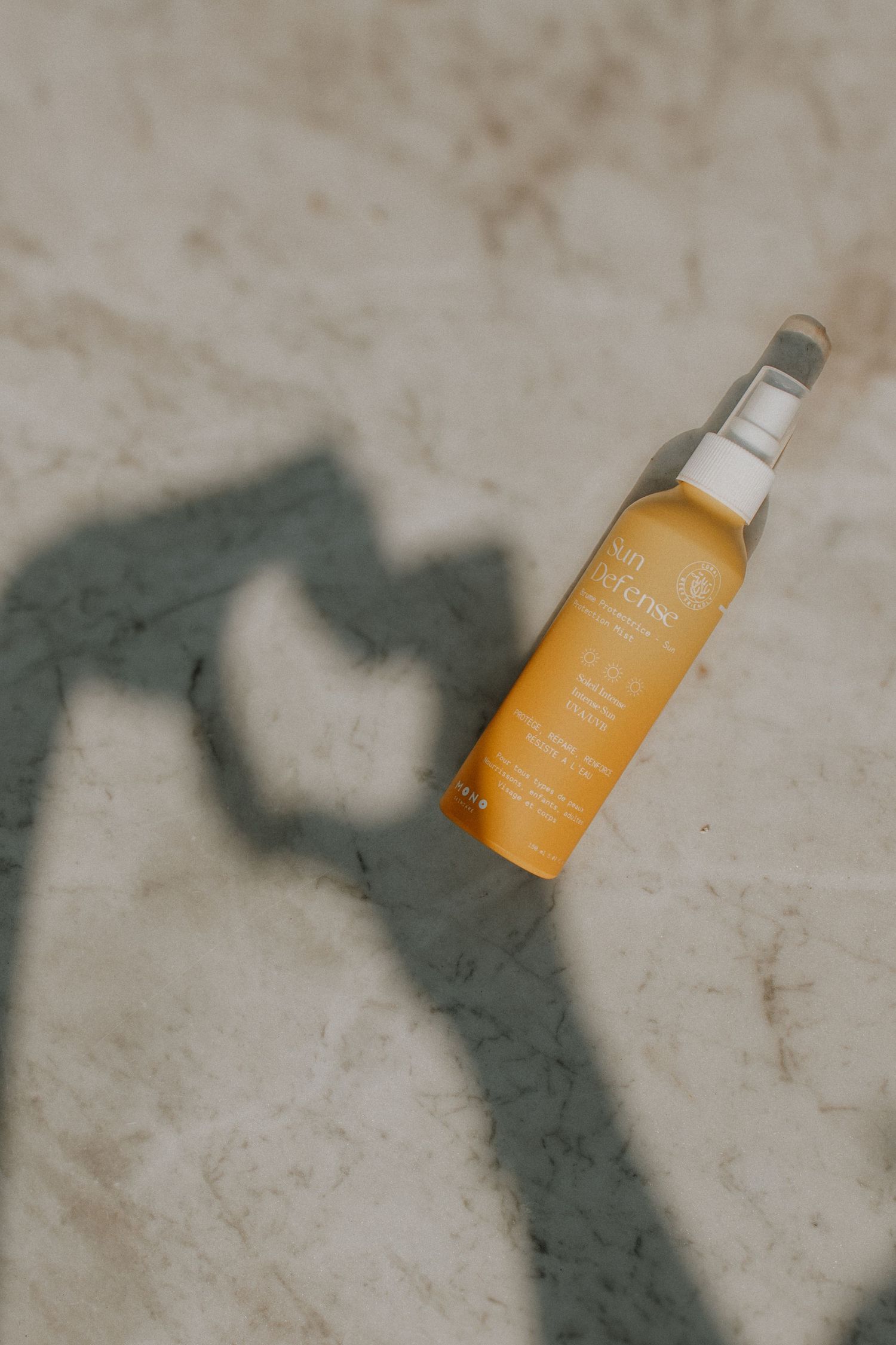 Yellow hair oil bottle on marble surface with heart-shaped shadow in the background.