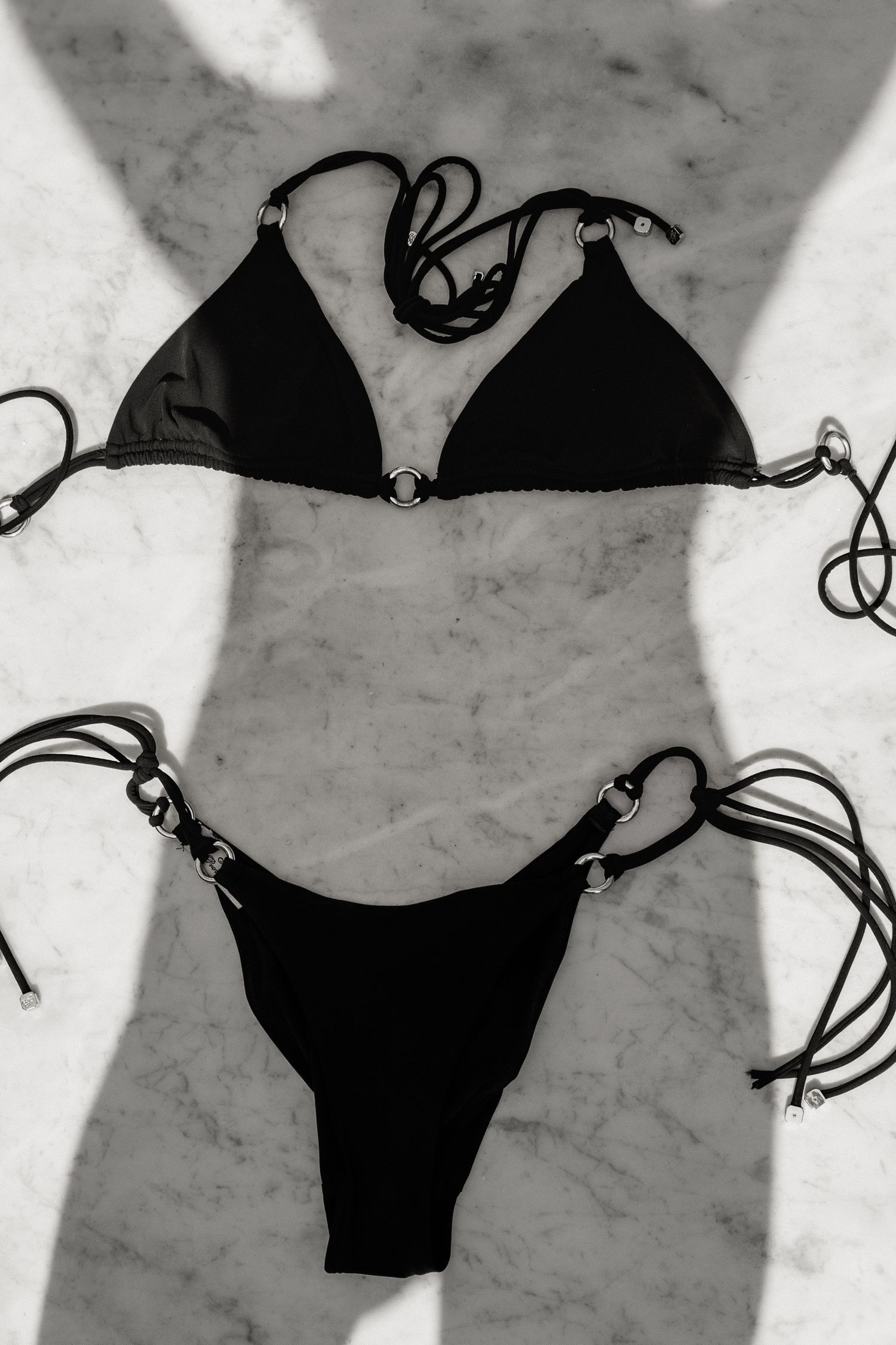 Black triangle bikini set with silver ring hardware and tie sides, displayed flat on marble surface.
