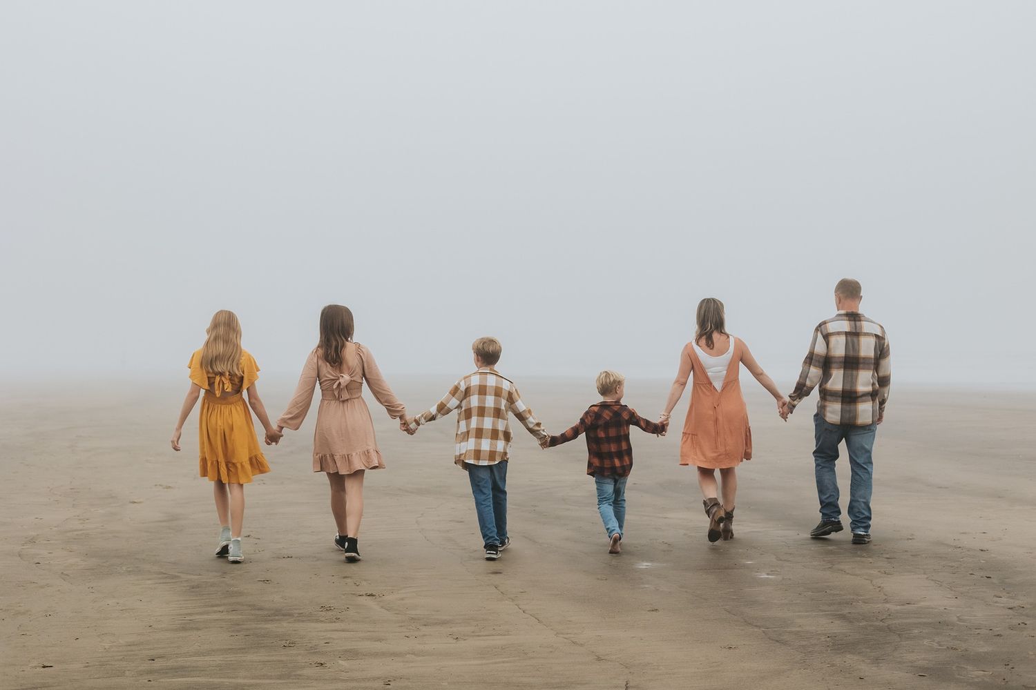 A family holds hands and walks away together at a beach in San Diego.