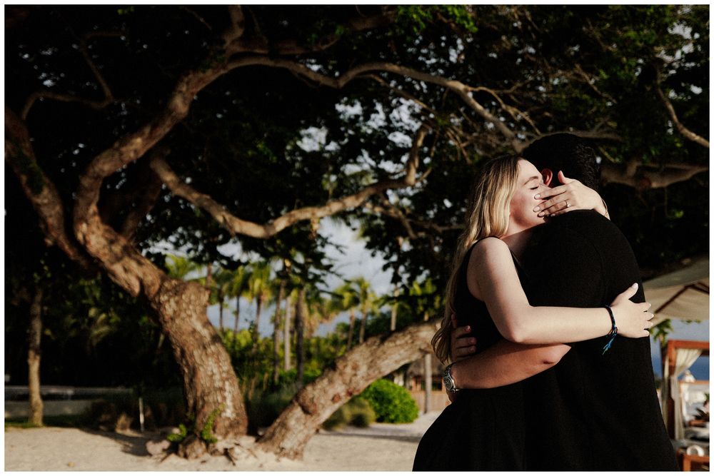Couple sharing a kiss during their beach engagement photos in Punta Mita beneath tropical trees at sunset.