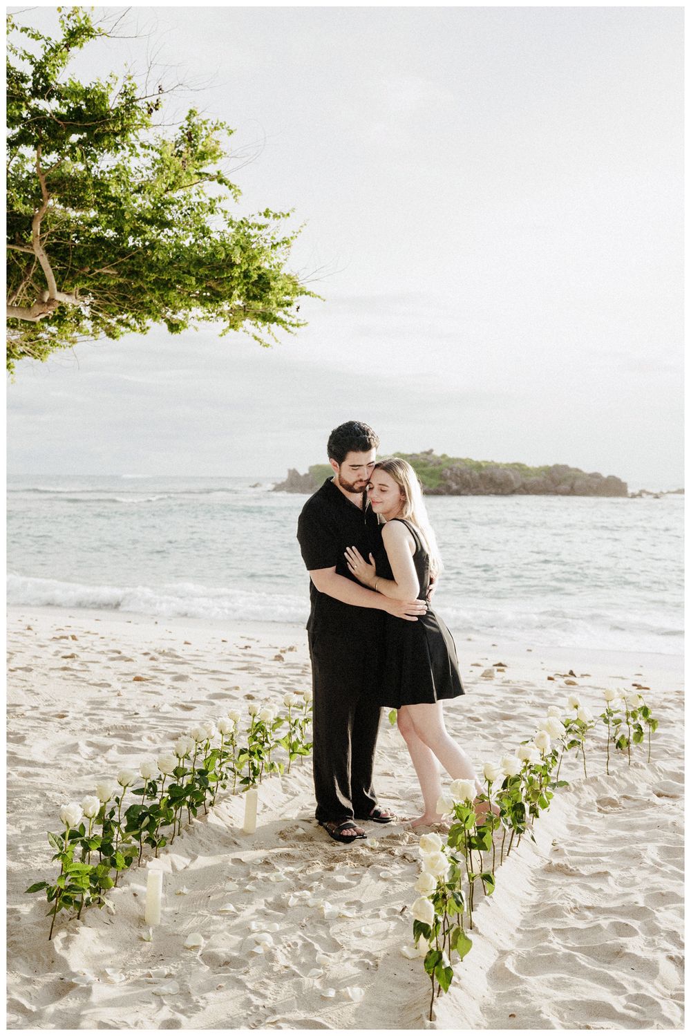 Couple embracing during a luxury engagement session in Punta Mita on a white sand beach with floral details and ocean views.