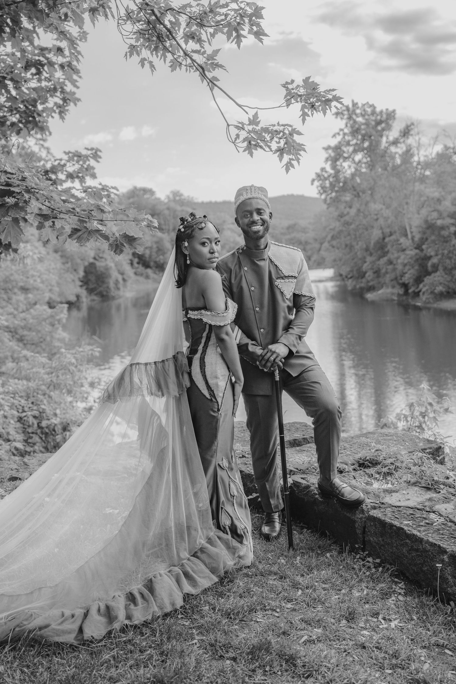 A couple in wedding attire dances together on a scenic path surrounded by greenery in black and white photography.