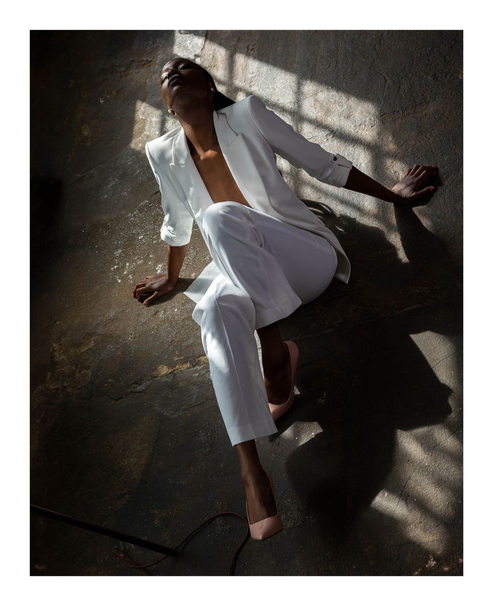 Fashion portrait of a woman in a white suit reclining on a surface in dramatic sunlight.