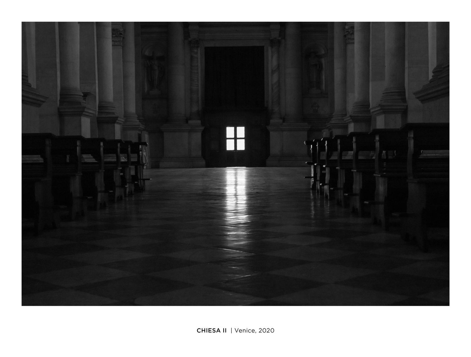 Black and white photo of a dark church interior in Venice, 2020, with pews and a glowing window at the altar.
